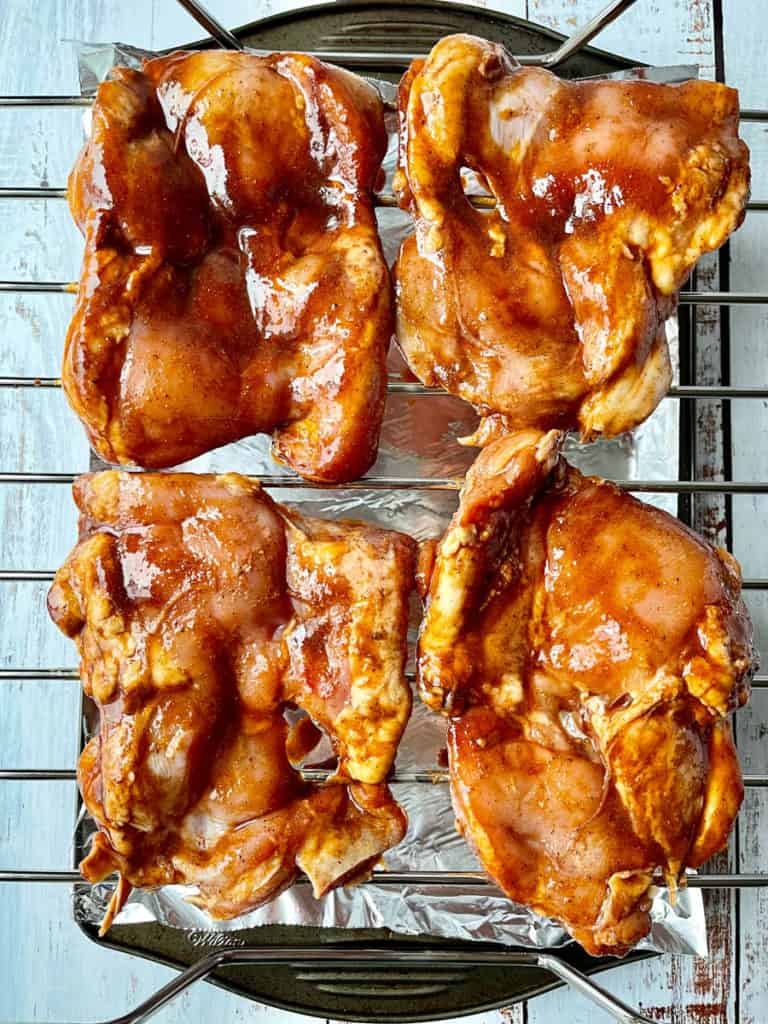 Chicken thighs marinated in char siu sauce on a rack ready to be baked.