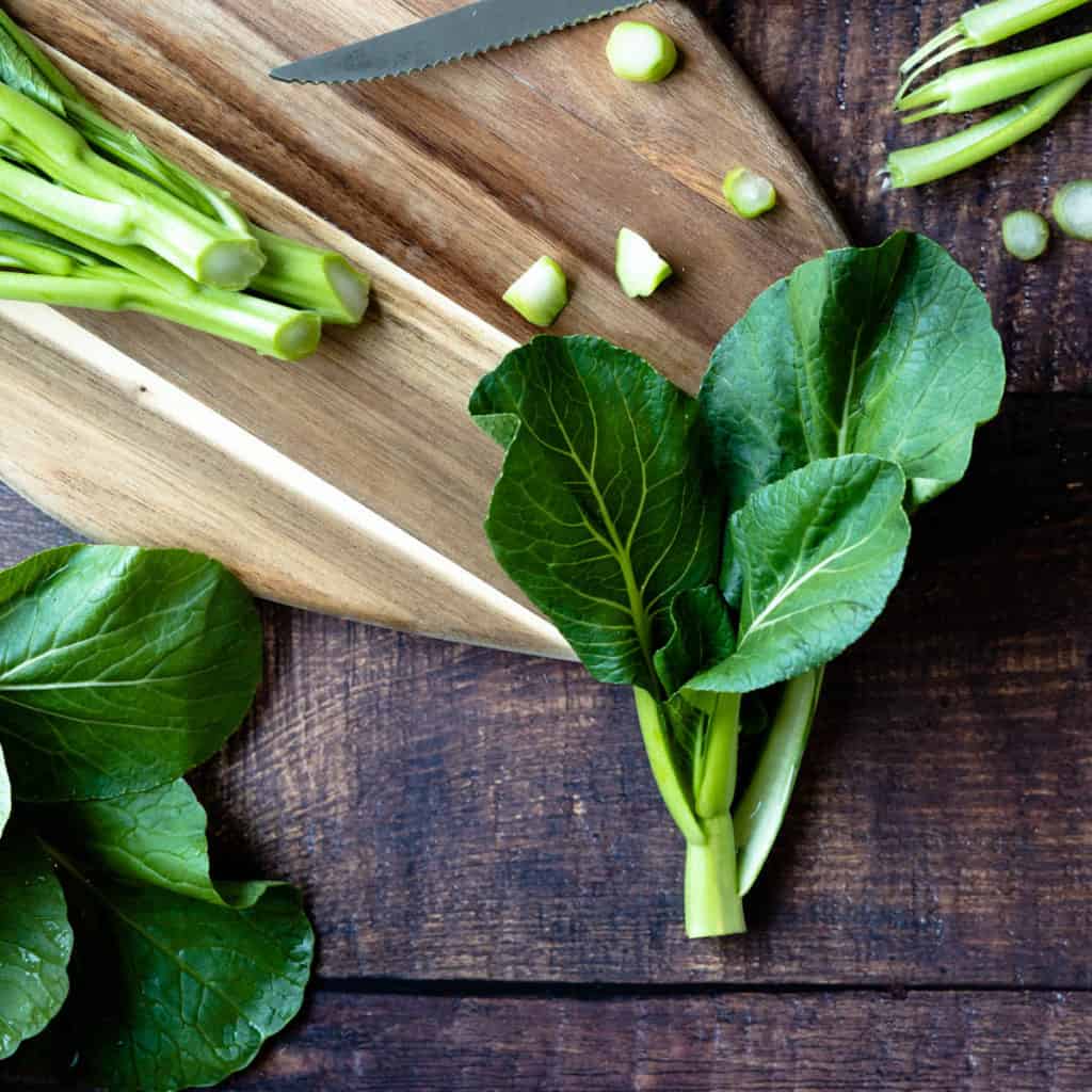 Uncooked yu choy stem on a cutting board.