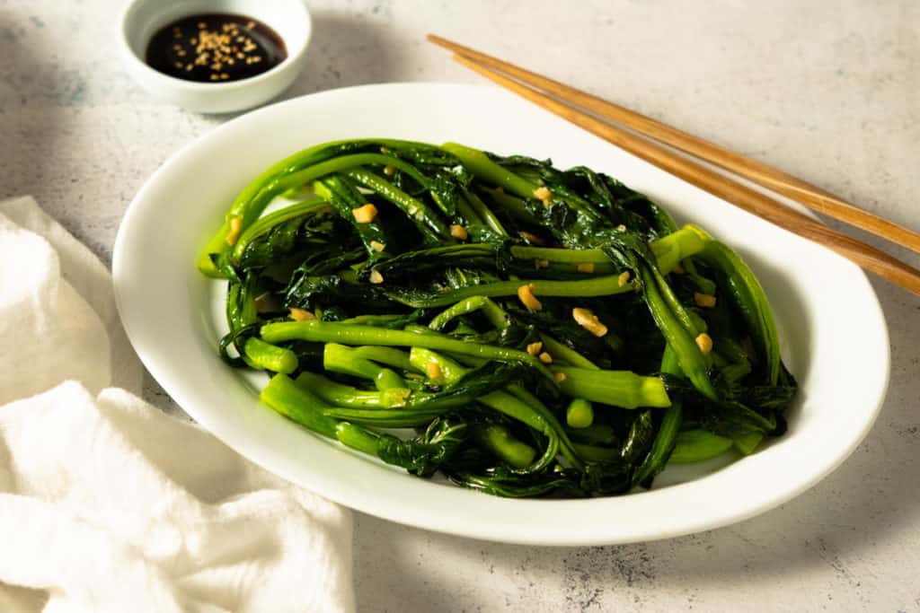 Stir fried yu choy on a family style plate with chopsticks.