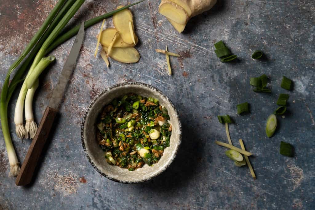 Ginger scallion sauce in a bowl with scallions and raw ginger surrounding it.
