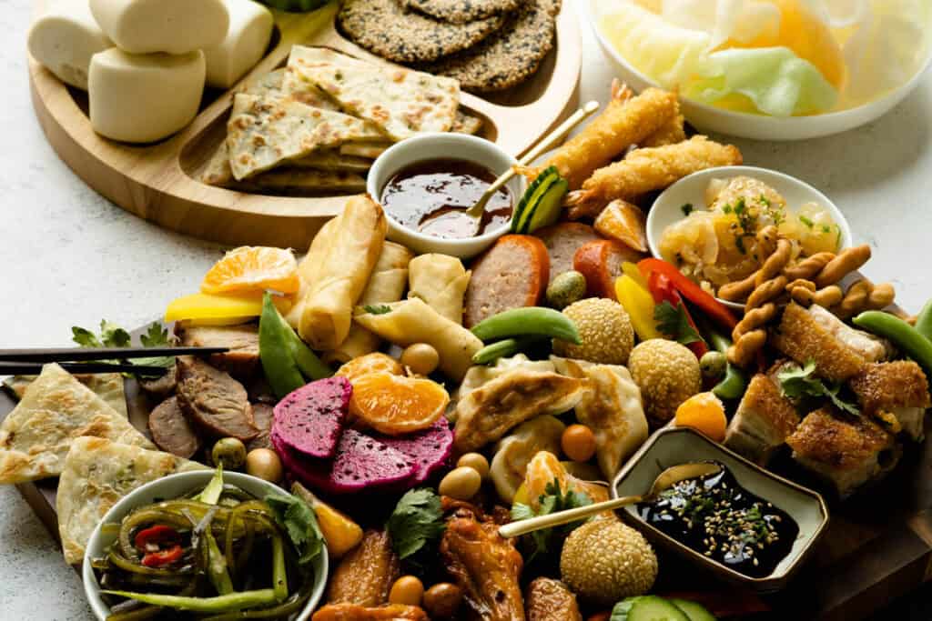 Asian charcuterie board with char siu, roasted pork, fruits and Asian snacks.