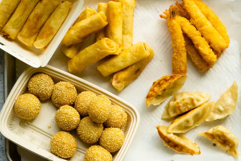 A display of Asian snacks such as spring rolls, pot stickers, sesame balls and shrimp tempura.