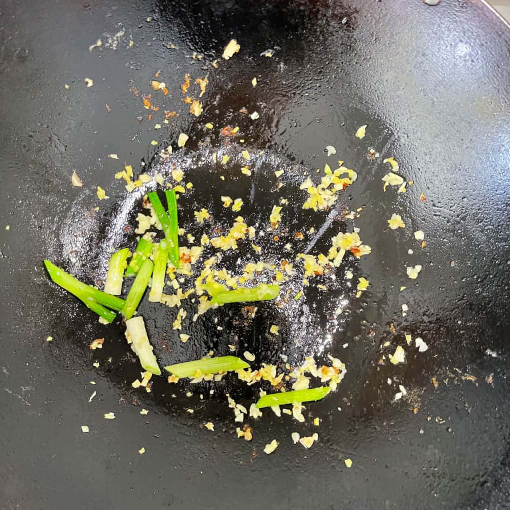 Aromatics of green onion, garlic and ginger heating in oil in a wok.