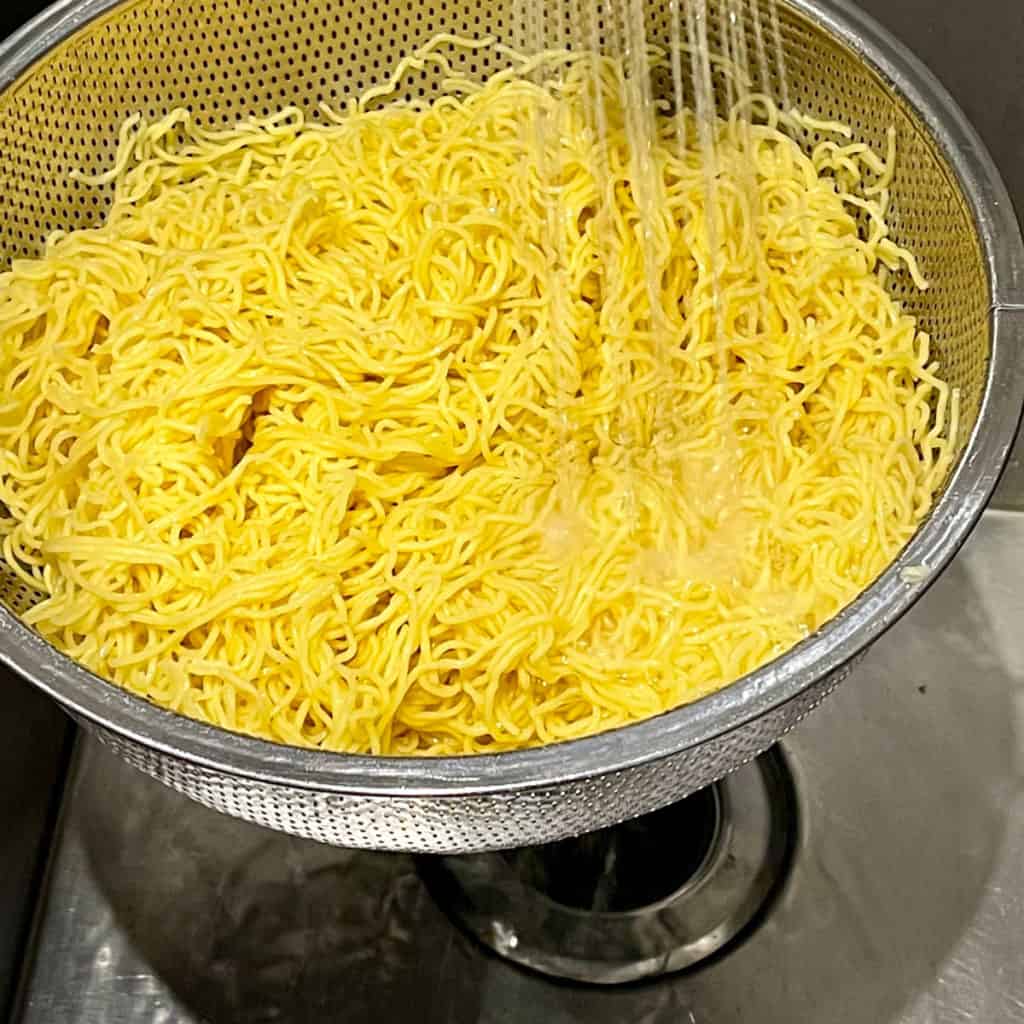 Blanched chow mein rinsing under cold water in a colander.