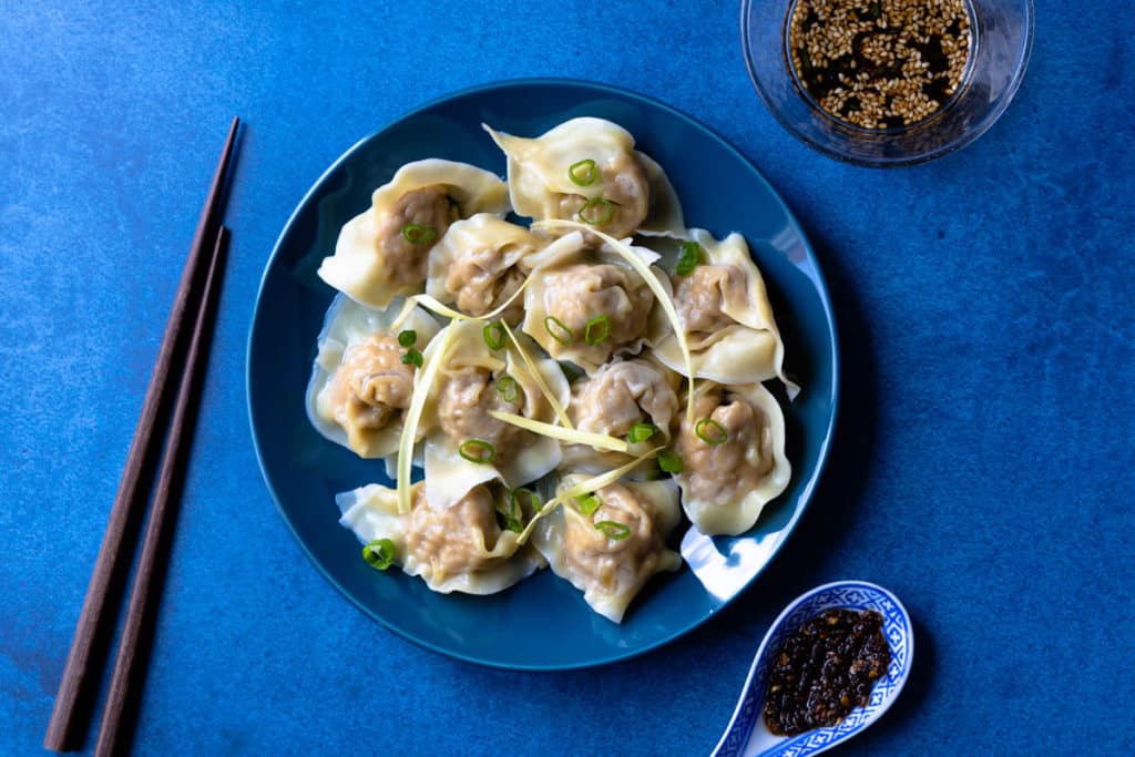 Plate of pork wontons with dipping sauce on the side.