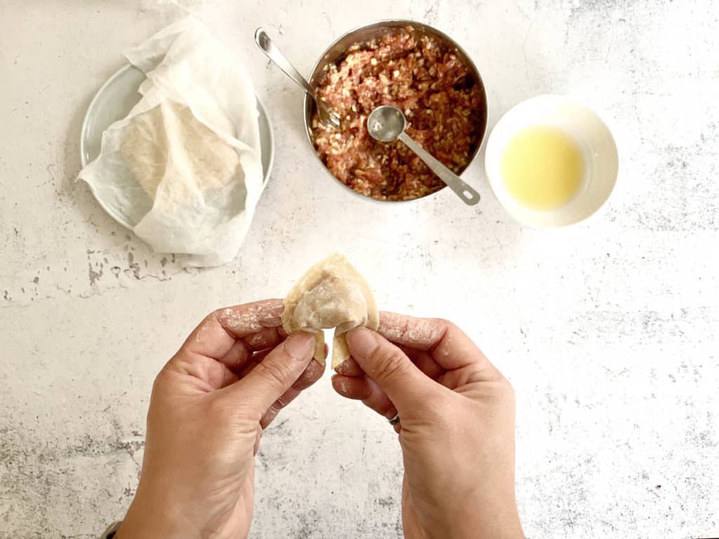 Wonton wrapping technique of combining the two corners and sealing them together.