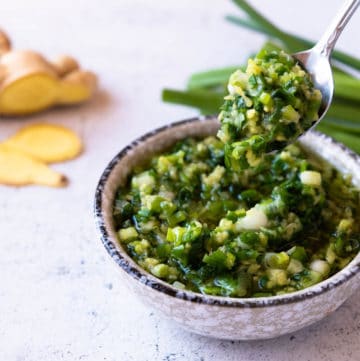 Spoon of ginger scallion sauce dripping from a bowl.