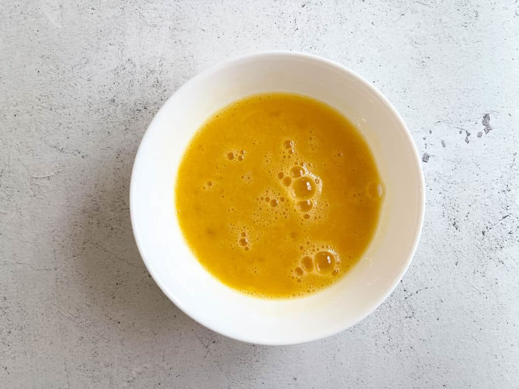 Beaten eggs in a bowl after 15 minutes with darker yellow color.