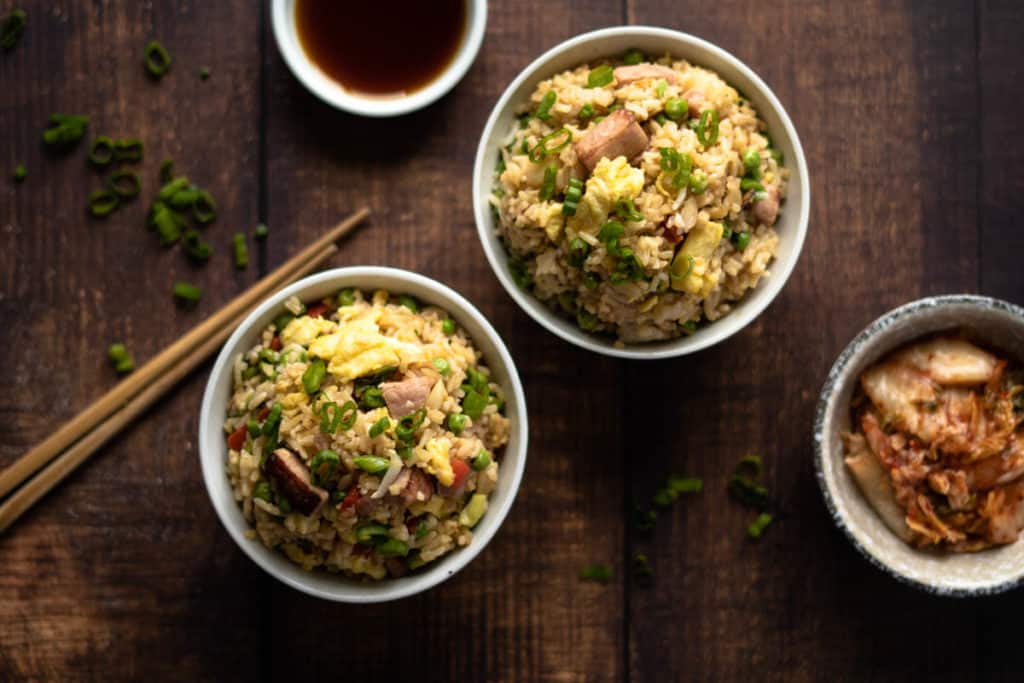 Two bowls of spam fried rice with kimchi and soy sauce.