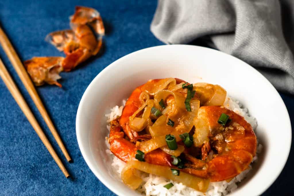 Shrimp with ketchup sauce and onions on top of a bowl of rice.