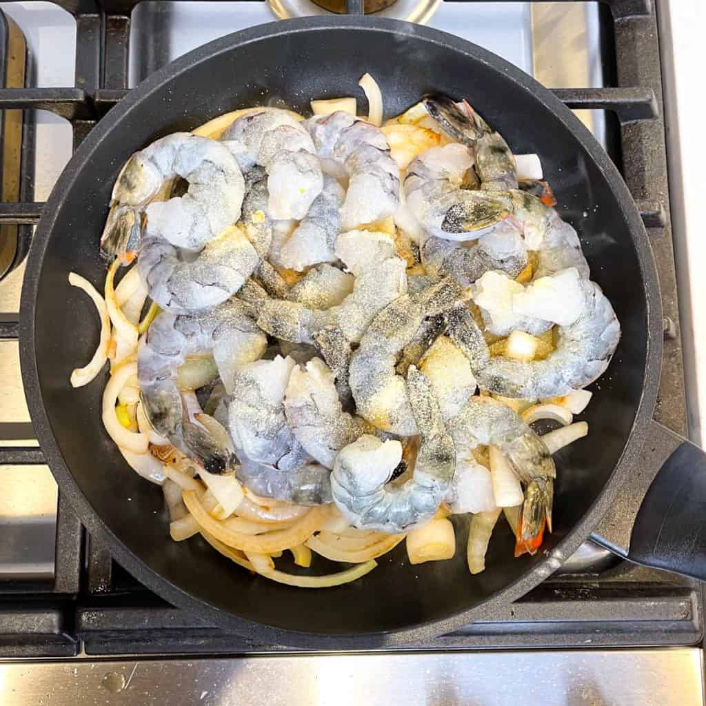 Shrimp searing in a pan with onions.