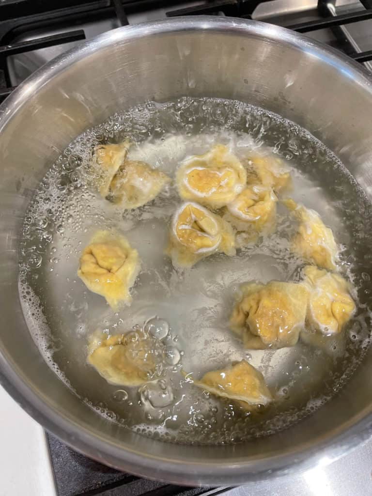 Wontons cooking in pot beginning to float up.