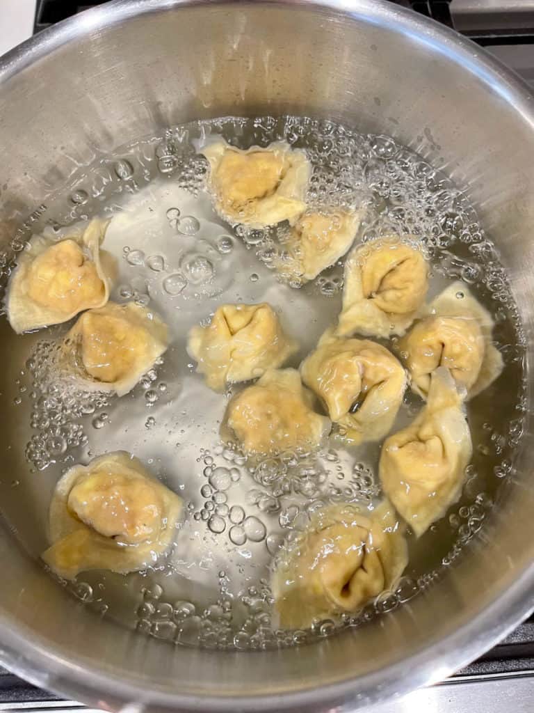 Fully cooked wontons floating in boiling water.