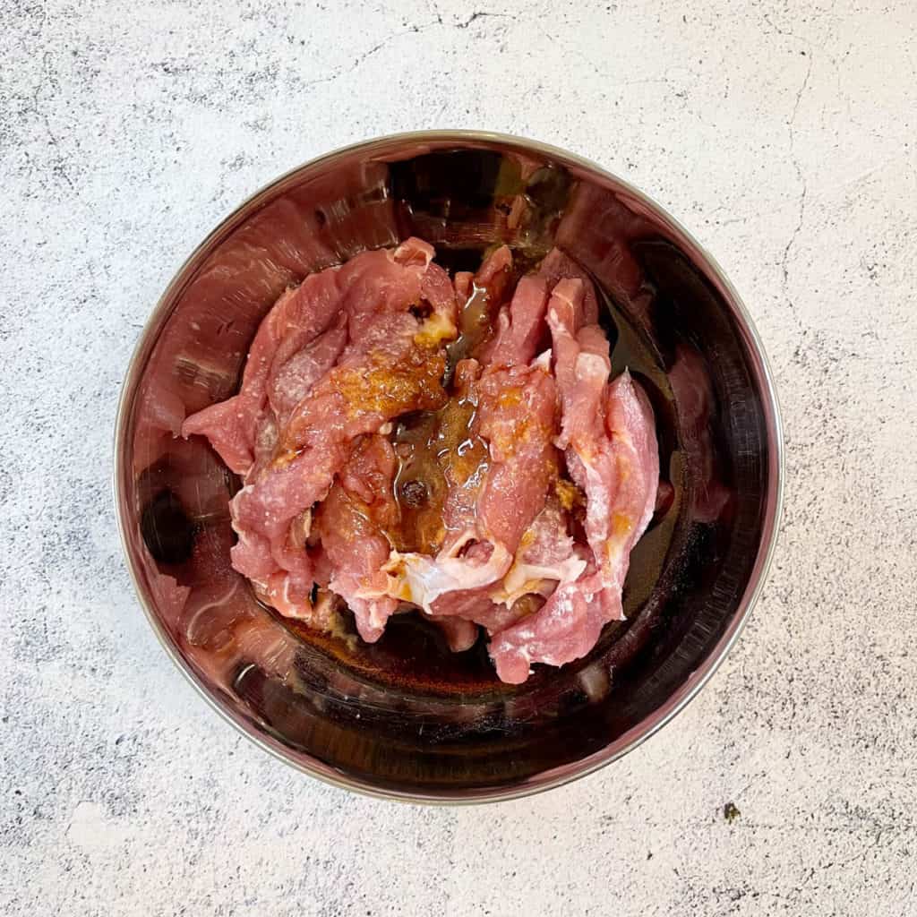 Slices of pork with marinated ingredients in a bowl.