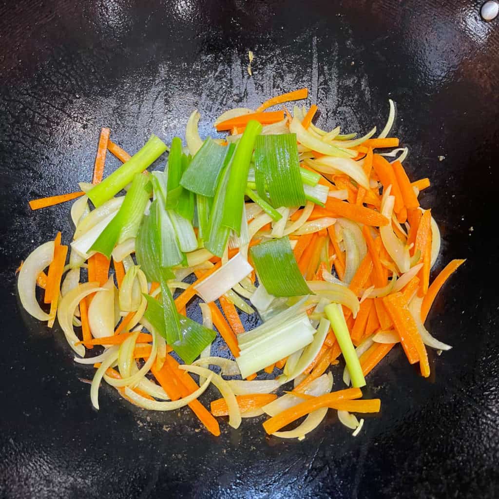 Carrots, onions and scallions stir frying in a wok.