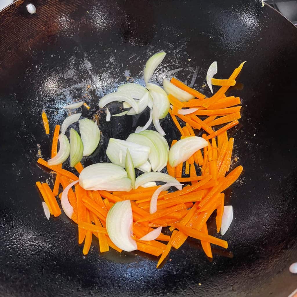 Sliced onions and carrots frying in a wok.