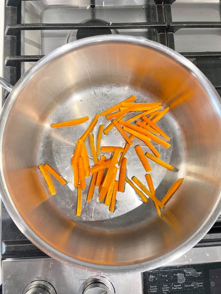 Carrot matchsticks sautéed in a pot.