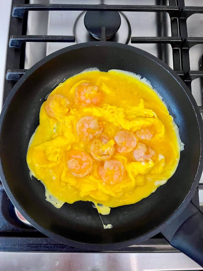 Scrambled eggs solidifying with shrimp in a pan.