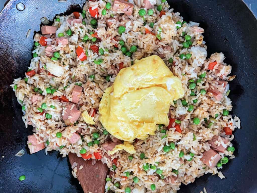 Egg scramble added to spam fried rice in a wok.