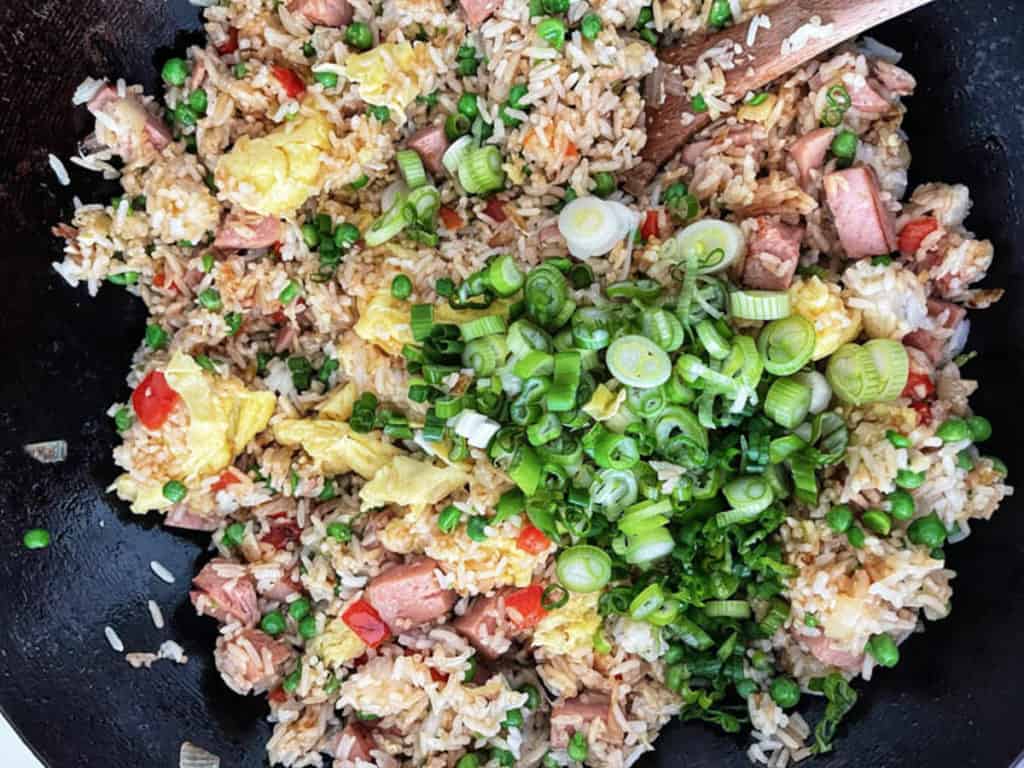 Chopped scallions added to spam fried rice in a wok.