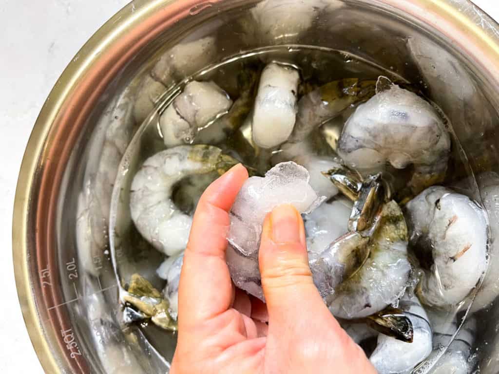Frozen shrimp defrosts quickly with water.  Ice chunks coming off the frozen shrimp.