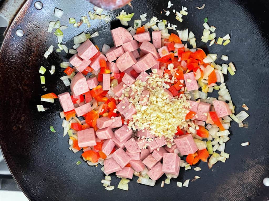 Frying onions, garlic, spam and red bell pepper in a wok.