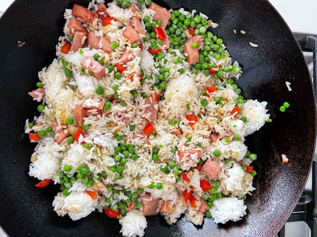 Spam fried rice cooking in a wok with cooked rice added.