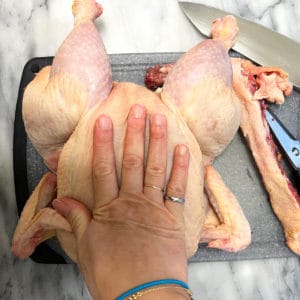 Flattening a raw chicken using your palm.