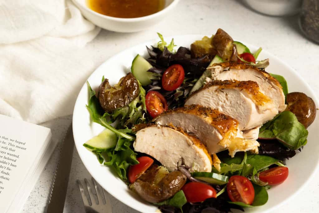 Roast chicken breast slices on a plate of salad.