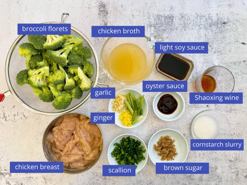 Broccoli chicken stir fry ingredients laid out including broccoli, chicken, broth, soy sauce, oyster sauce, Shaoxing wine, sugar, aromatics and cornstarch slurry.