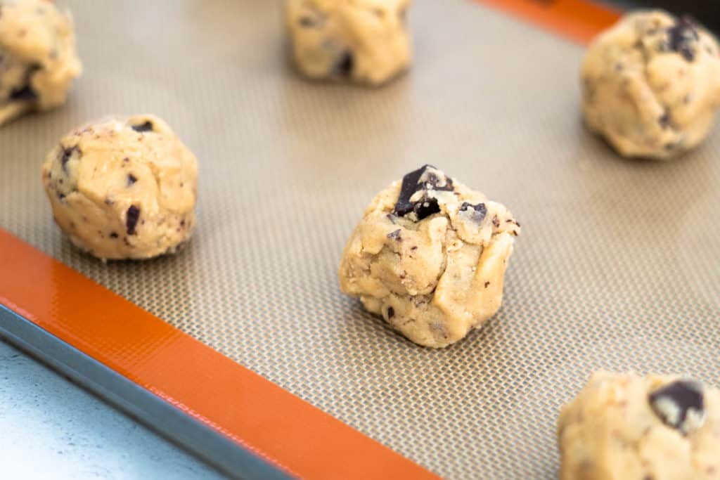 Chocolate chip cookie dough without baking soda or powder rolled into balls and placed on baking sheet.