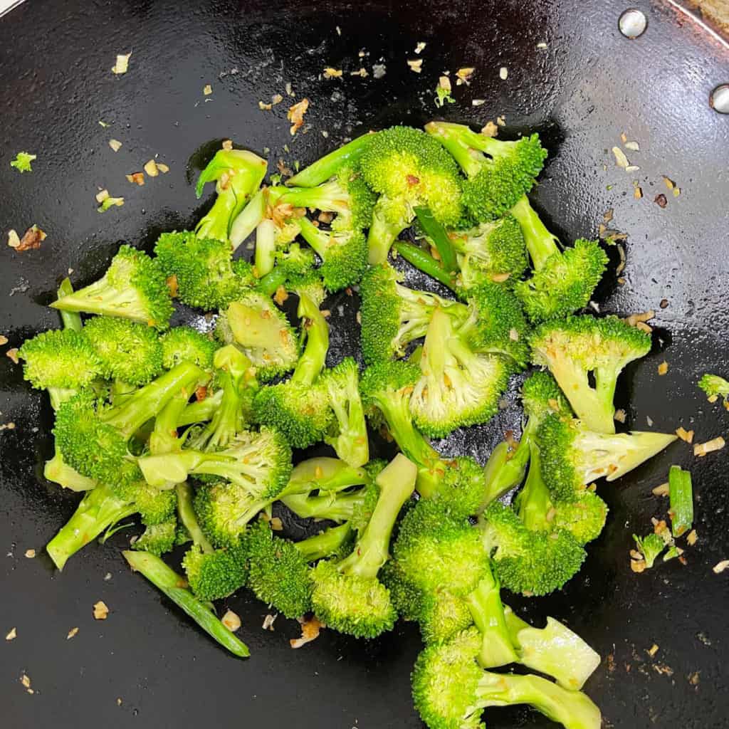 Broccoli florets stir frying in a pan.
