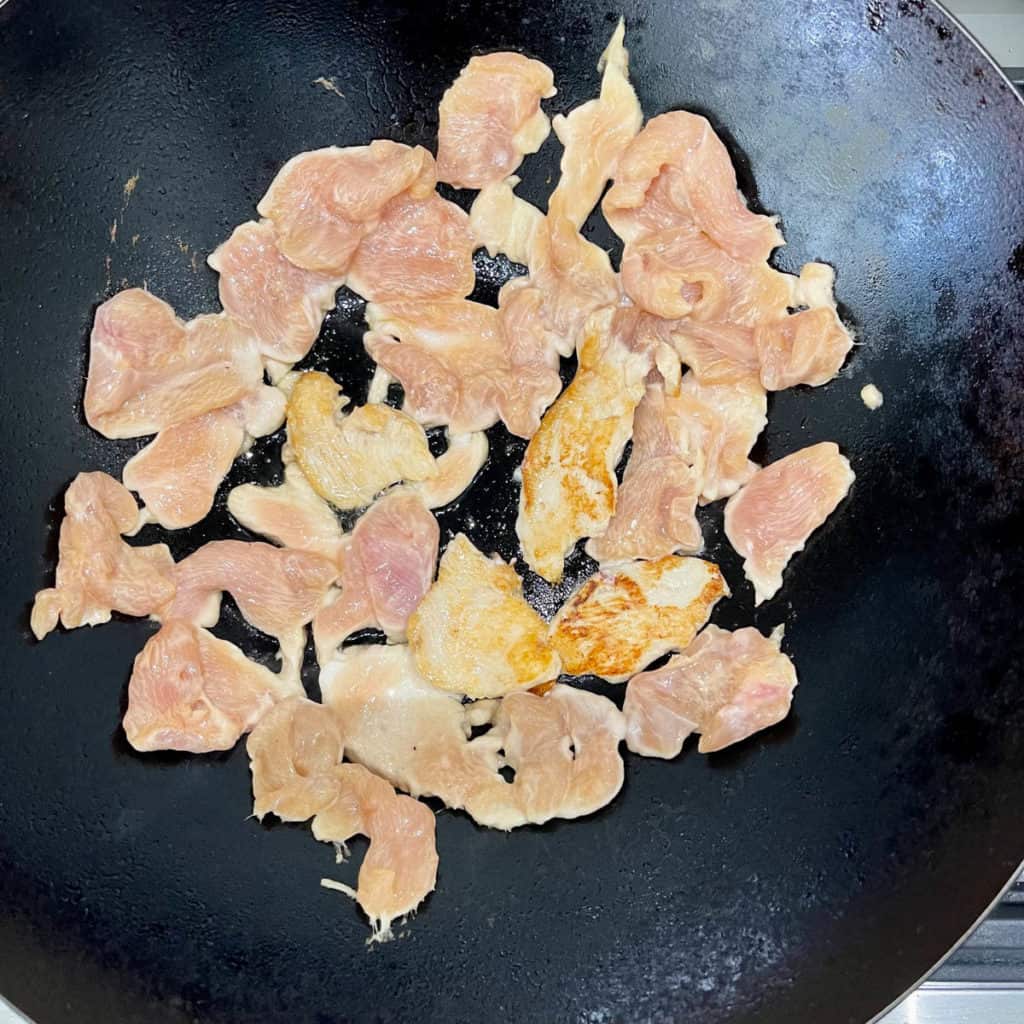 Pan seared slices of chicken breast in a wok.